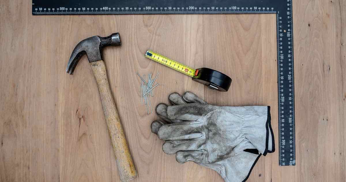 Hamer, winkelhaak, rolmeter en werkhandschoenen op een houten werkblad