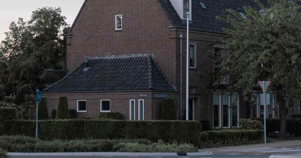 Bakstenen woning met pannendak aan een straat met bomen