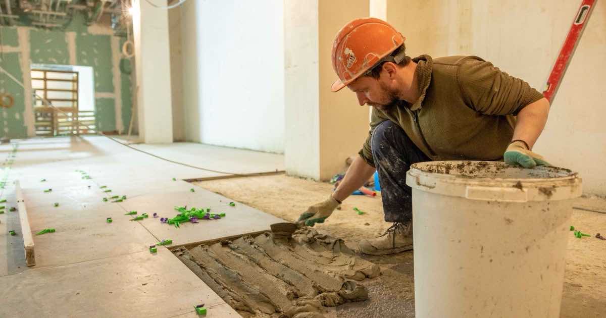 Vakman met helm legt vloertegels in een ruimte in renovatie