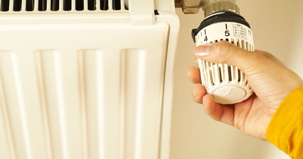 Hand draait aan de thermostaatkraan van een witte radiator