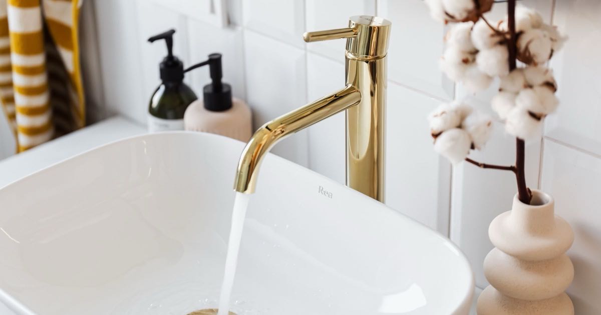 Water stroomt uit een gouden kraan in een witte wastafel